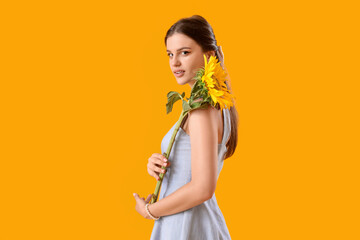 Young woman with beautiful sunflower on yellow background