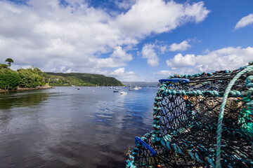 A serene landscape featuring a body of water with boats and buildings along the shore. The image captures a peaceful scene with a cloudy sky overhead.  Portree, Scotland, isle of skye