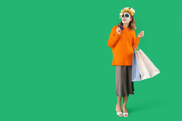 Young woman with painted skull, credit card and shopping bags on green background. Mexico's Day of the Dead (El Dia de Muertos) celebration