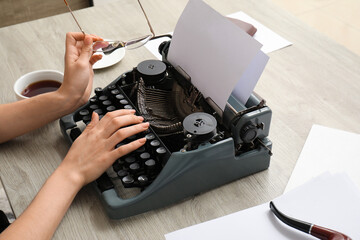 Woman typing on vintage typewriter at beige wooden table