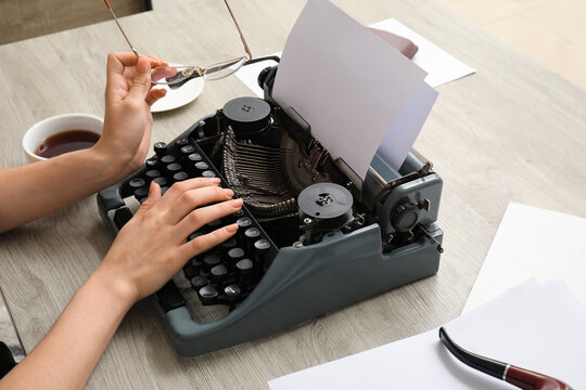 Woman typing on vintage typewriter at beige wooden table