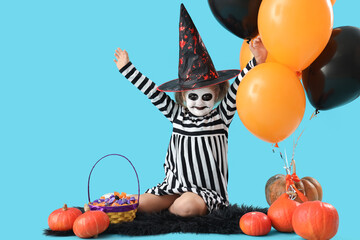 Little girl dressed for Halloween with candies and balloons on blue background