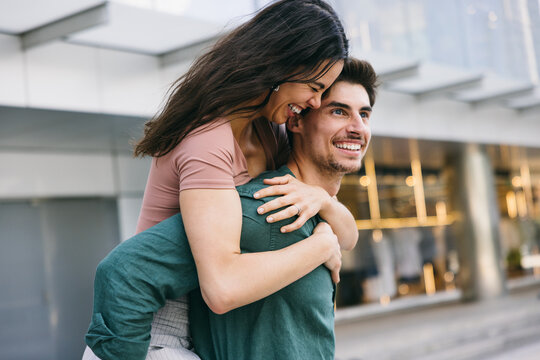 Joyful piggyback ride of a couple smiling in Azca, Madrid street