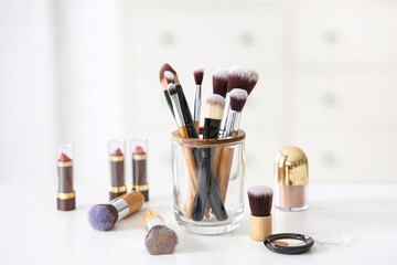 Makeup brushes with lipsticks and eyeshadows on white table at home