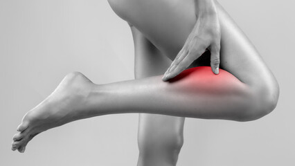 Woman touching her calf suffering from sudden leg cramp, feeling pain in torn or overstretched muscle. Rare rheumatism symptom or after overtraining at gym © Home-stock