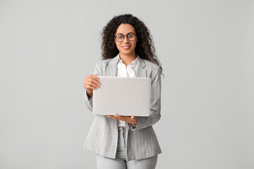 Fototapeta premium Young African-American businesswoman with modern laptop on grey background