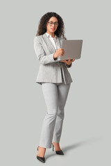 Fototapeta premium Young African-American businesswoman with modern laptop on grey background