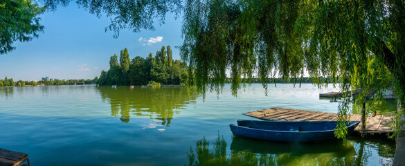 Panoramic view of lake Herestrau with a blue boat on a dock under a wilow tree, King Michael I Park...