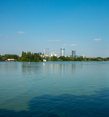 Fototapeta premium Skyline of modern Bucharest reflected on the the clear waters of Herastrau Lake, King Michael I Park, Bucharest, Romania