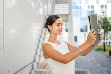 Fototapeta premium Young woman stand in front building and have video call on tablet