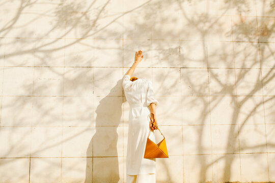 Elegant Woman in White Dress with Orange Purse Against Wall