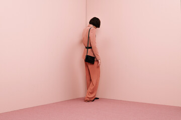 Woman Standing Alone in Pink Room with Black Bag