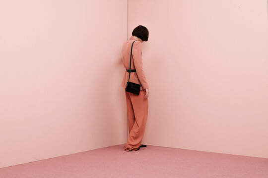 Woman Standing Alone in Pink Room with Black Bag