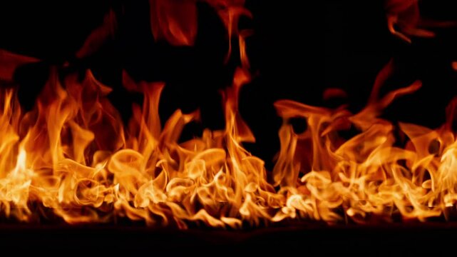 Beautiful dancing fire, the surface is ablaze. Lots of fire. Close-up immersion in the flames. The camera passes through the fire. Burning tongues of flame on a black backdrop in slow motion