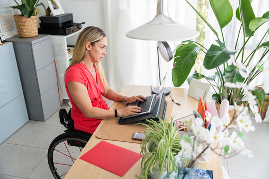 Professional woman in wheelchair typing on laptop in home office