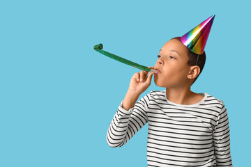 Cute little African-American boy in party hat with whistle celebrating birthday on blue background