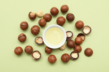 Bowl of macadamia oil and nuts on green background