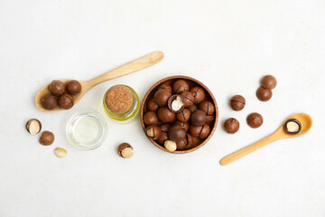 Bottle of macadamia oil, wooden spoons and bowl with nuts on light background