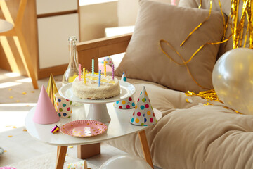 Birthday cake with party decor on table in messy living room
