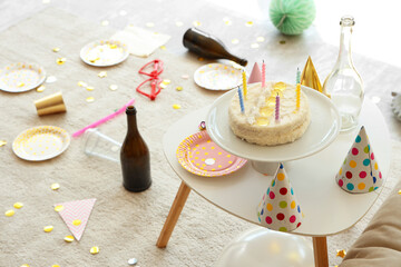 Birthday cake with party decor on table in messy room, closeup