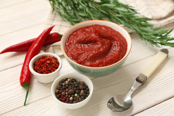Bowl of chili sauce and different spices on white wooden background