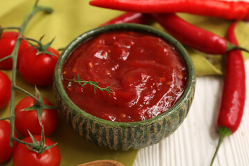 Bowl of chili sauce with fresh peppers and tomatoes on white wooden background