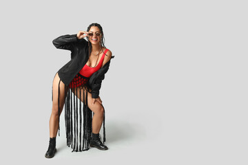Stylish young African-American woman with dreadlocks on grey background