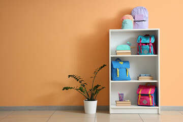 Shelving unit with books and backpacks near orange wall