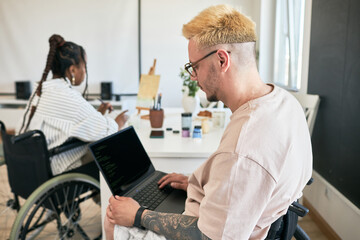 Team of coworkers collaborating in modern inclusive office utilizing laptops and technology Wheelchair users engaging in productive tasks wearing casual attire