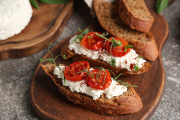 Wooden board of tasty tomato bruschetta with ricotta on grey background