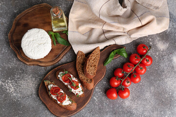 Wooden board of tasty tomato bruschetta with ricotta and basil on grey background