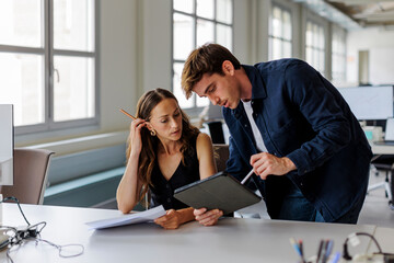 Manager explaining work task using digital tablet in busy office