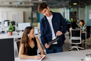 Manager explaining work task using digital tablet in busy office