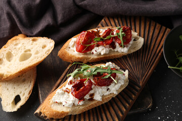 Wooden board of tasty tomato bruschetta with ricotta and arugula on black background, closeup