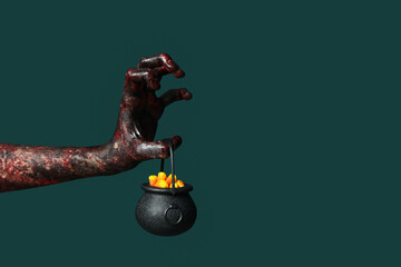 Hand of zombie with cauldron on green background. Halloween celebration