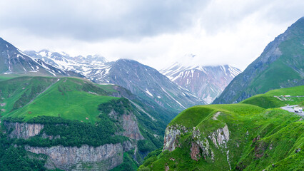 Panoramic view from the grassy hill on the Kazbek mountains and the green valley crossed