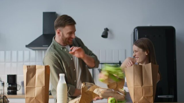 Laughing spouses unpacking groceries in home kitchen fooling together closeup.