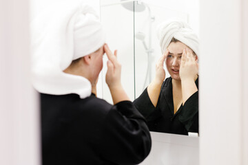 Woman with towel on head applying face cream with two hands 