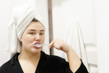 Close-up photo of woman with towel on head brushing teeth
