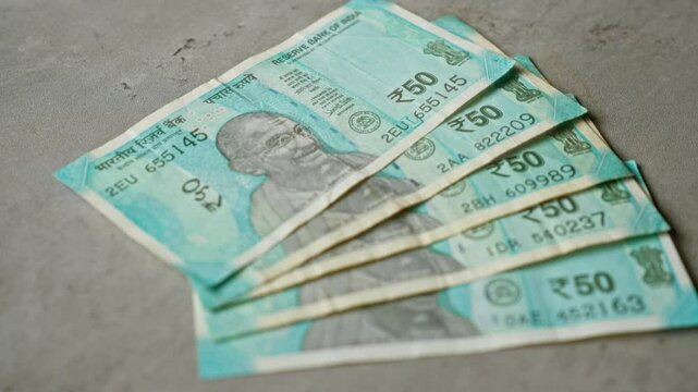 Indian rupee banknotes spread across a concrete surface, showcasing the vibrant 50 rupee notes featuring mahatma gandhi's image.