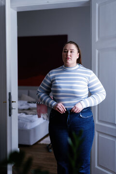 Plus size woman putting on clothes in front of bedroom door
