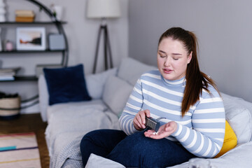 Plus size woman taking pills from pill organizer sitting on sofa