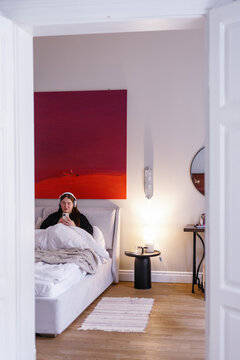 Woman in pajamas listening to music in wireless headphones in bed