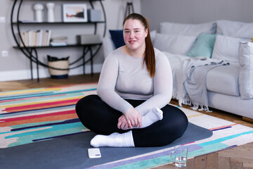 Portrait of plus size woman sitting cross-legged on floor in apartment
