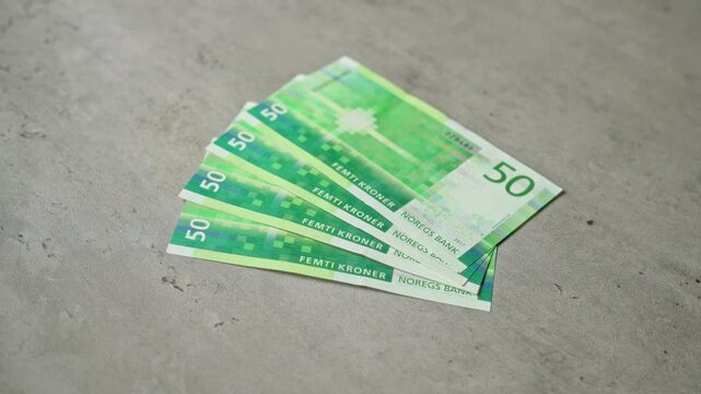 Norwegian 50 krone banknotes fanned out on a concrete surface showing vibrant green colors and security features.