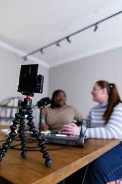 Close-up of camera in foreground with podcasters on blurred background