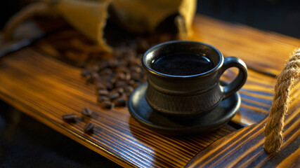 black cup with coffee and coffee beans on a wooden surface. Fully roasted coffee beans on a rough rustic wood surface with a freshly brewed cup of coffee. close-up