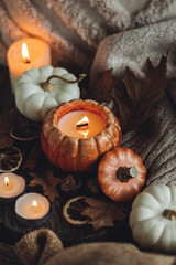 Autumn composition with burning candles, mini munchkin pumpkins, warm wool knitted sweater on the wooden windowsill. Dark colours. Cozy home atmosphere, Thanksgiving decor, fall inspiration. Close up