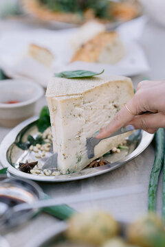 Slicing a large piece of white cheese topped with basil
