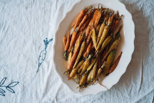Roasted baby carrots on a white oval plate, rustic setting.